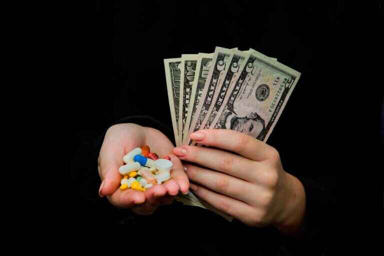 Money And Pills In Hands, Isolated On Black. Wasting Too Much Mo