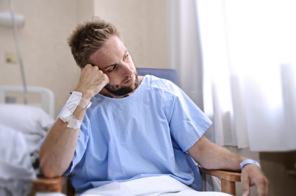 young injured man in hospital room sitting alone in pain worried