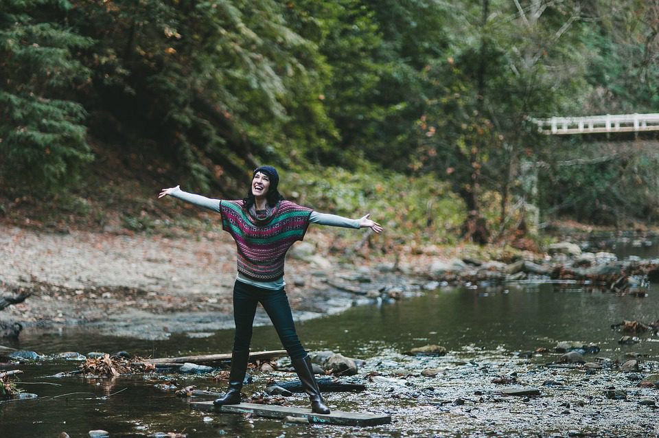 happy woman standing at forest river with raised hands