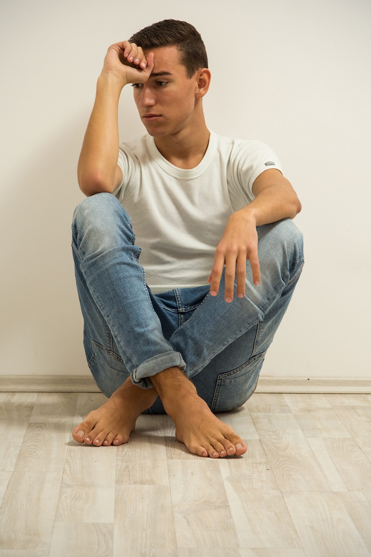 Young man sitting on a floor with hands on head.