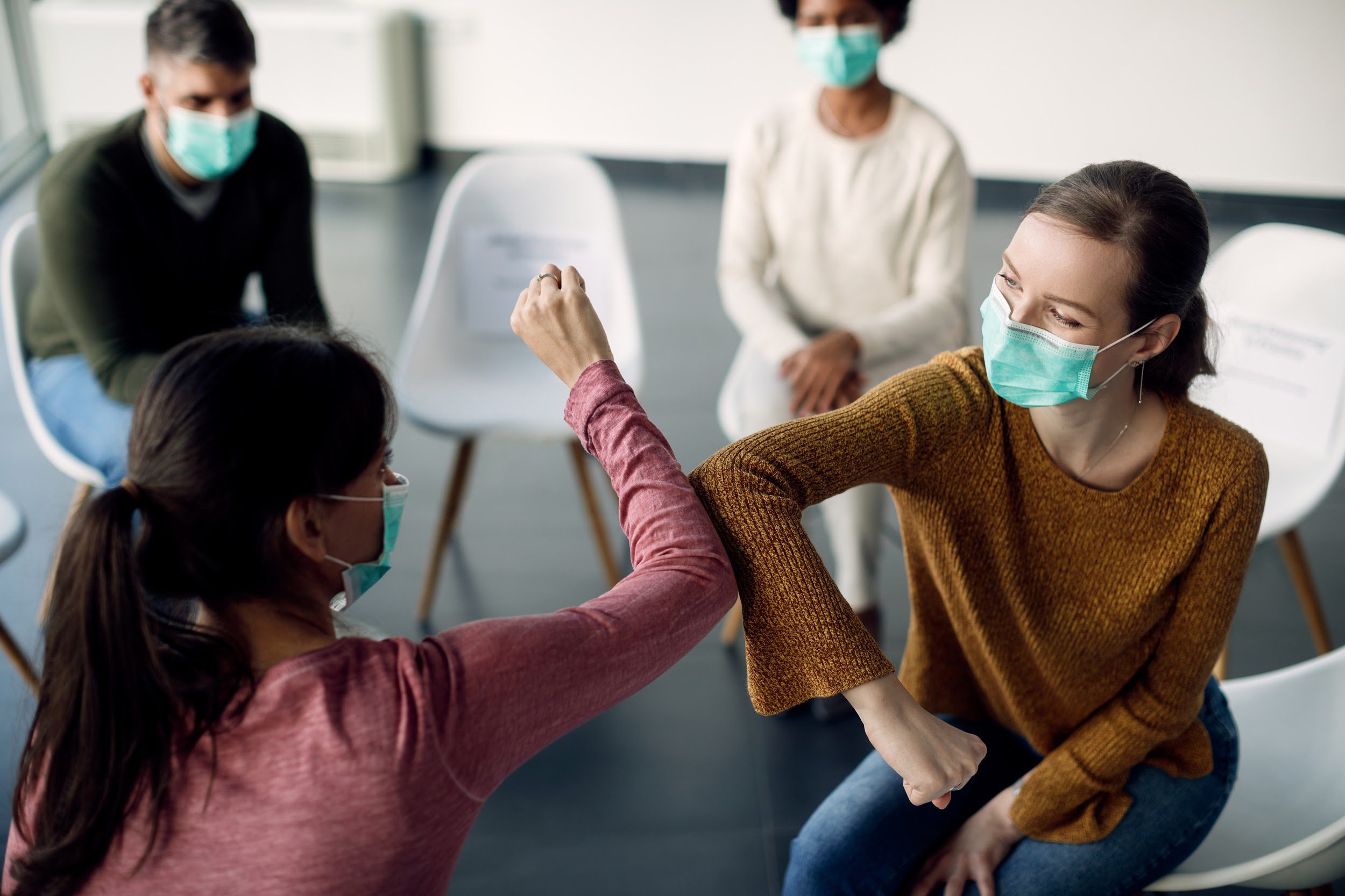 Female members of group therapy wearing face masks and greeting with elbows due to coronavirus pandemic.
