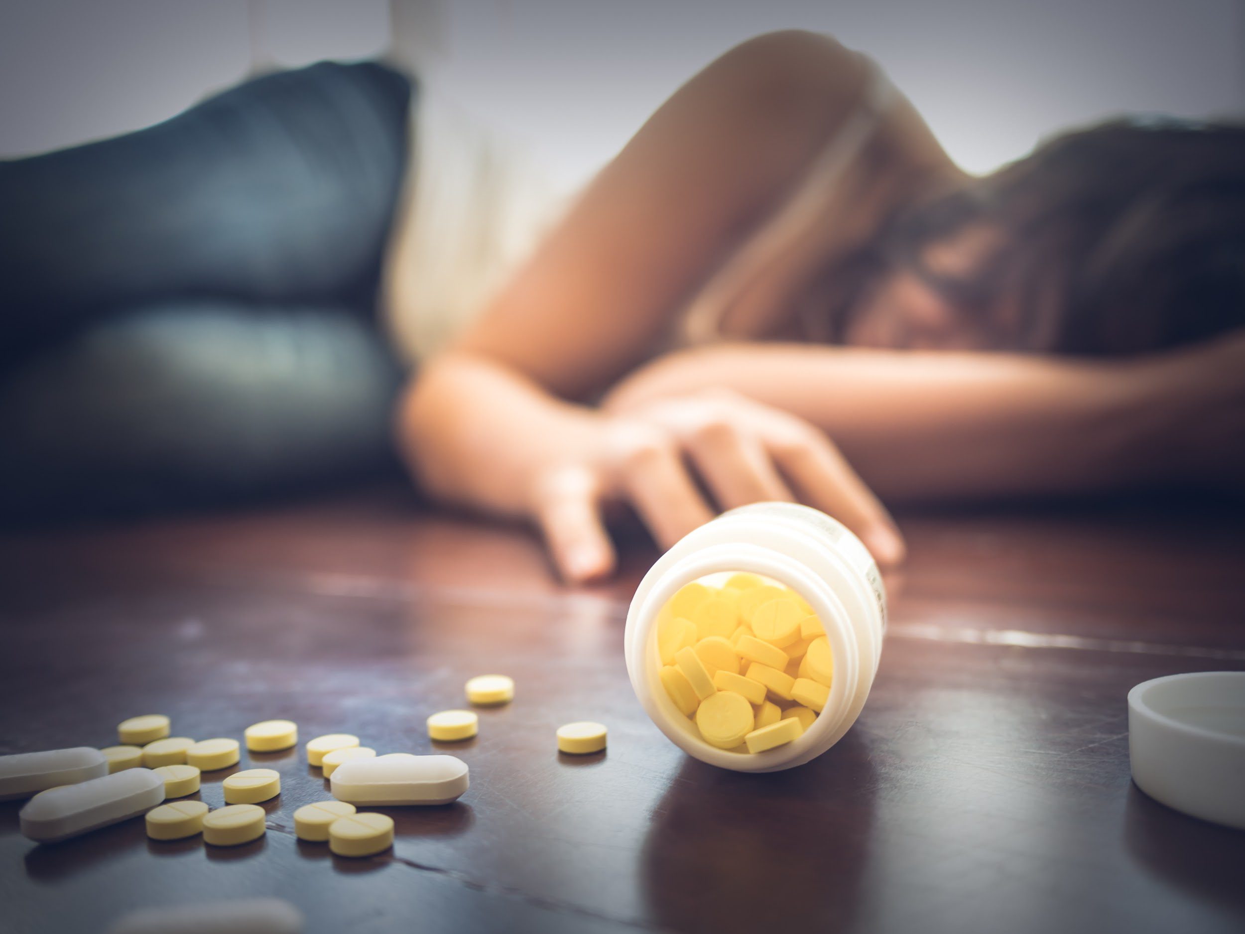 Woman taking medicine overdose and lying on the wooden floor with open pills bottle